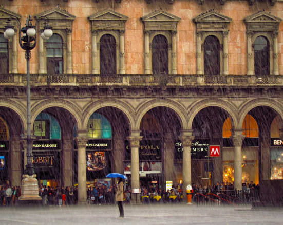 A lone woman admires the Milan Duomo under a blue umbrella in the Piazza during a thunderstorm 