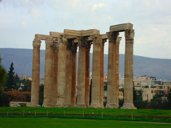 A group of Greek columns and mountains in the background