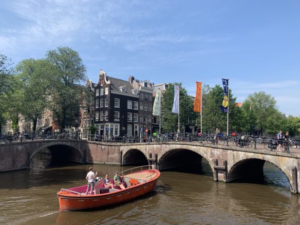 A small red boat about to pass under an arched bridge on the canal in Amsterdam