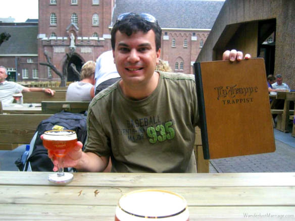 Alex with La Trappe beer and menu with the cafe and abbey in the background