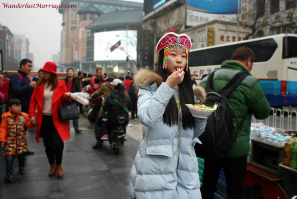 Girl eating noodles on the streets of Beijing, China