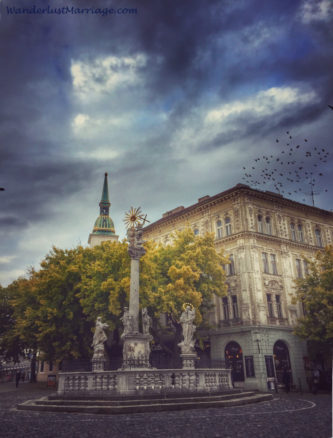 Statue in the square with birds in the storm sky