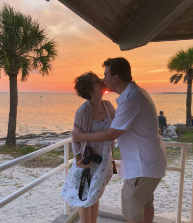 Alex and Bell kissing with sunset in the background on the aptly named Sunset Beach in Tarpon Springs, Florida