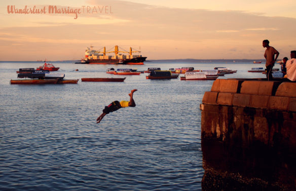 Kids diving off the sea wall into the ocean at sunset