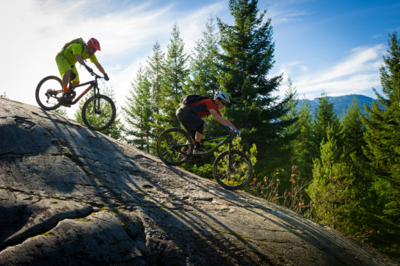 2 people mountain biking on a large rock