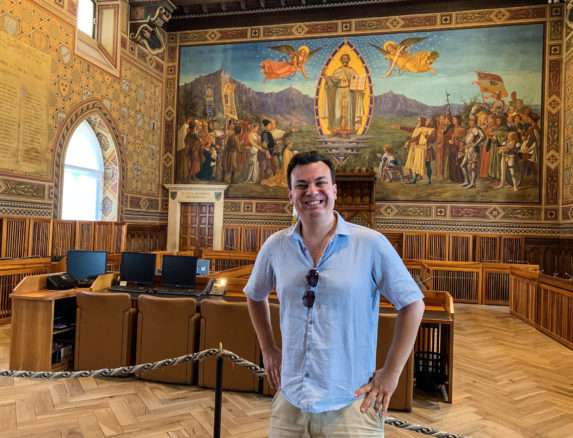 Alex standing in on of the city hall rooms with a fresco paining in the background