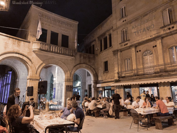 Village square at night with people sitting out and drinking