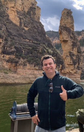 Alex on a boat on Big Horn river with the orange colored rocks rising up behind him