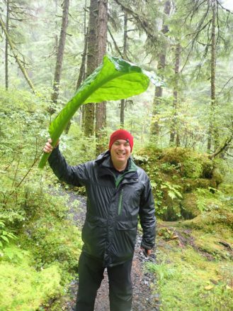 Alex in the forest using a large green leaf as a umbrella