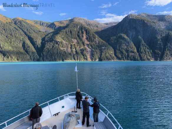 Front of boat, clean blue water and fjords under a blue sky in Alaska