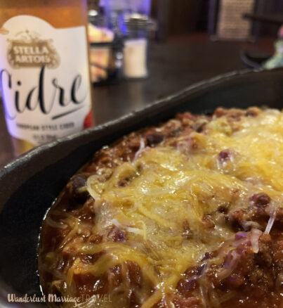 Bowl of chili topped with cheese and a beer