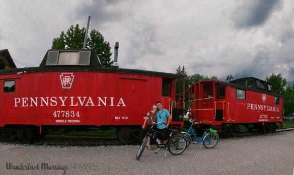A red train with Pennsylvania printed on the side car and Alex and Bell with 2 bicycles 