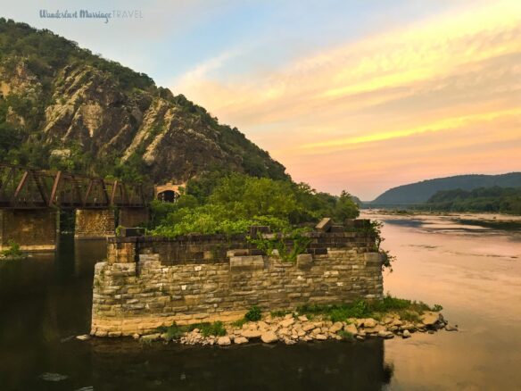 Picture of a river at sunset with a train line running across the river into the mountain