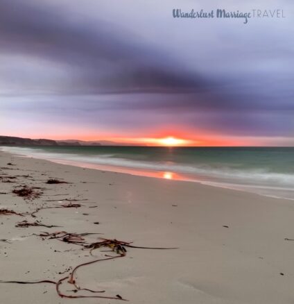 Beach at sunset with purple clouds and cliffs off in the background