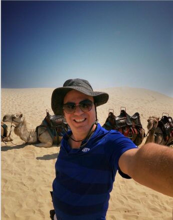 Alex taking a selfie in front of a pack of camels in the sand dunes of Anna Bay, NSW