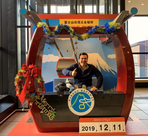 Alex Kallimanis giving thumbs up inside a prop Hakone Ropeway cable car at Owakudani