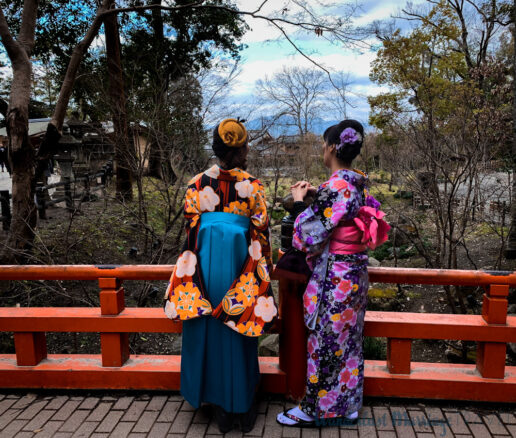 two Japanese women standing on a bridge in Kyoto wearing traditional kimonos