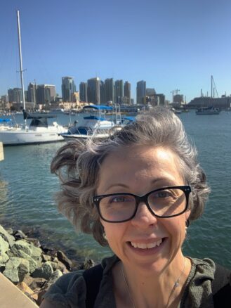 Women with glasses with the bay behind her with boats and skyscrapers 