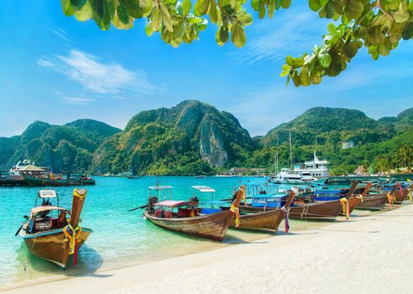 Small wooden boats docked on the shore of the beach, with aqua water, and rocky fjords coming out of the ocean