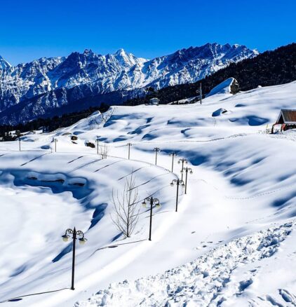 Mountains covered in thick white snow, you can see a couple of small homes poking out of the snow