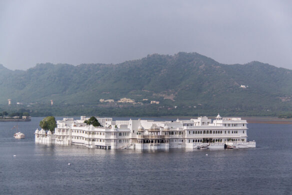 A large white hotel surrounded by a large lake and green mountains in the background