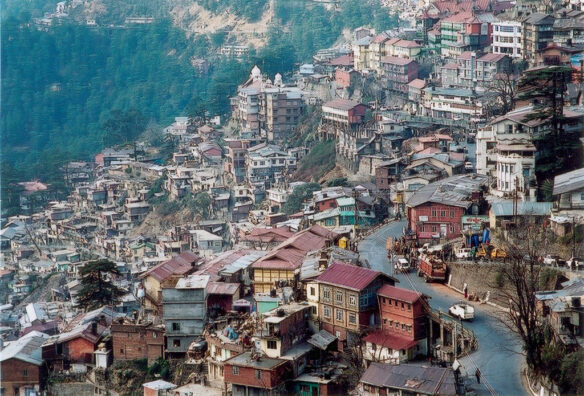 A large village on the side of the mountain with a green forest on the outskirt of the village