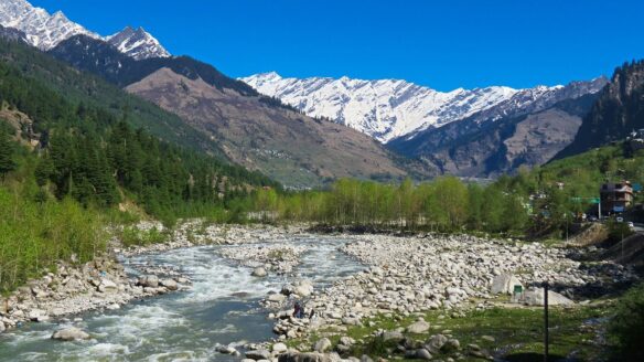 River flowing through a snow capped mountain range with a rocky river bank