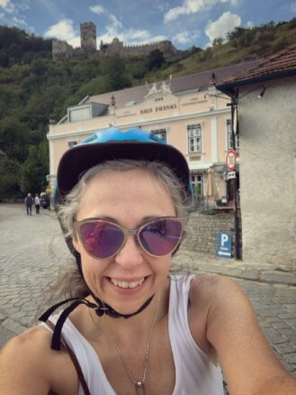 Bell takes a selfie in her bike helmet and behind her is a castle a top a hill