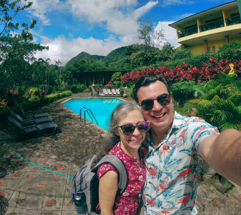 Alex and Bell selfie with the hotel pool behind us as well as the building and then the lush garden, golden frig statues and mountains