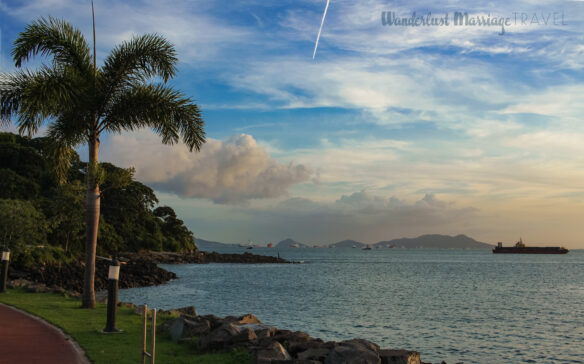 View of the entrance into the Panama Canal, boats are off in the distance waiting to enter, and there are mountains in the background
