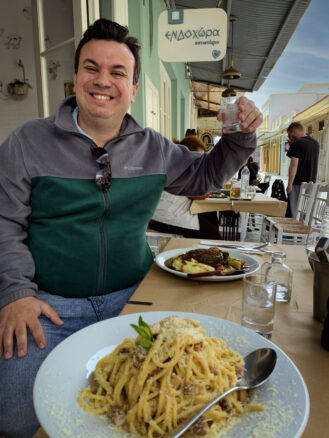 Alex raising a glass of tsiporou over lamb and pasta lunch at Endochora Restaurant in Andros Chora, Greece