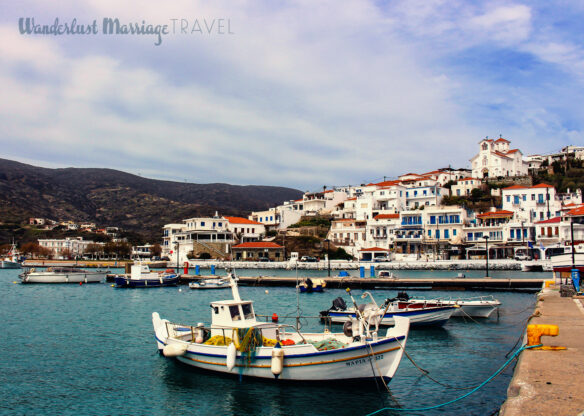 The marina of Batsi on the island of Andros, Greece - with small boats, whitewashed houses and a church above town.