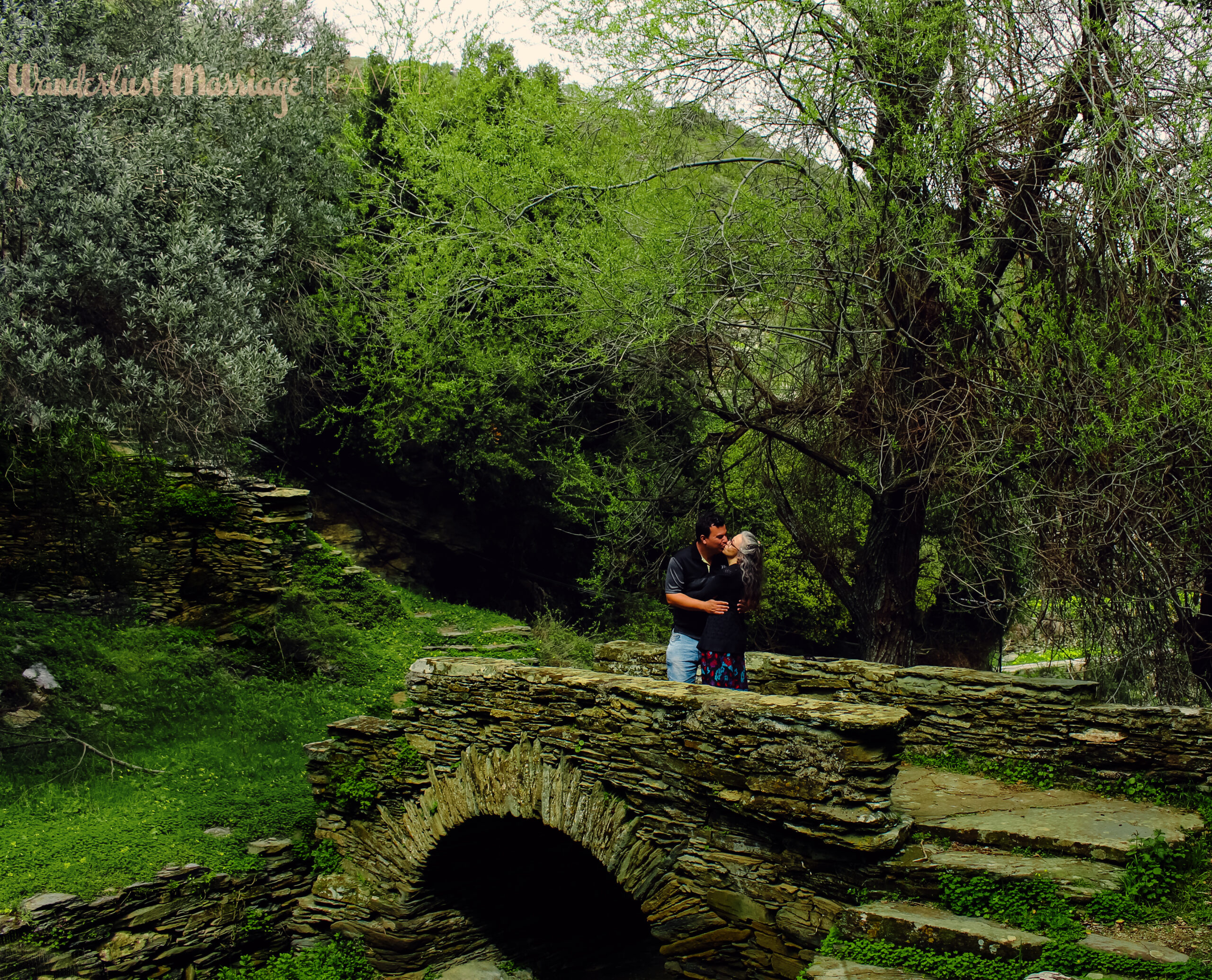 Stone bridge nestled in lush green scenery and a man and a lady kiss while standing on the stone bridge
