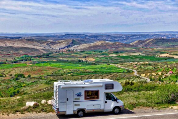 A motorhome parked along a scenic road with a view of a scenic landscape with small mountains and green grass