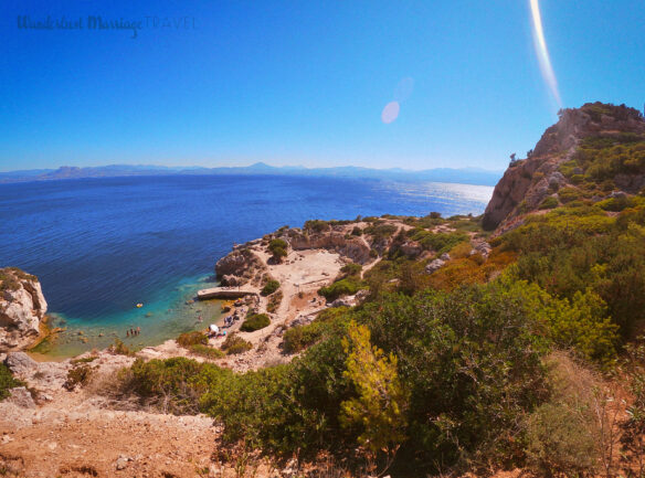 from the top of the cliff looking down at a small bay where people are swimming in crystal clear water, with blue skies