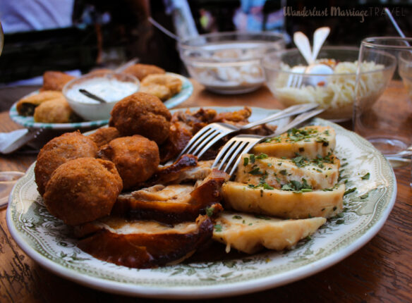 Plate on a table with meat balls, pork and dumplings, and sides of potato salad and sauerkraut 