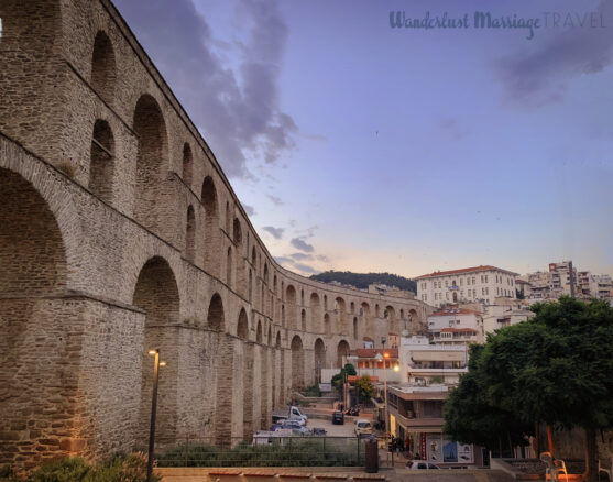 Large stone aqueduct structure and the town of Kavala in the background at dusk