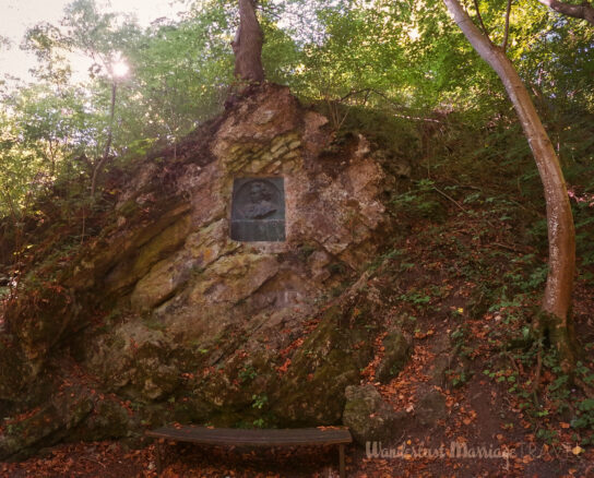 Plaque with bust of Beethoven embedded into the rock and a park bench in the woods