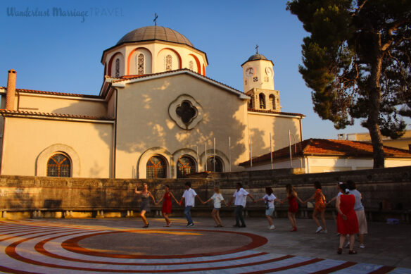 A group of locals circle dance in the square with a church in the background