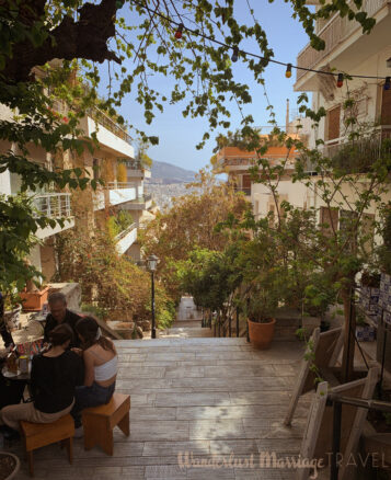 Top of a pedestrian stairway in Kolonaki overlooking Athens, people sit at a small cafe table on a day with blue skies