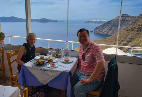 Alex and Bell sit at a table with a Greek salad and a view 