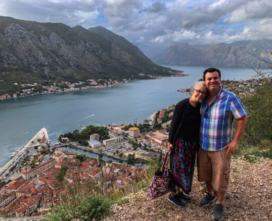 Alex and Bell stand above the romantic town of Kotor with the sea and mountains behind them