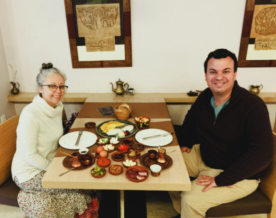 Alex and Bell sit a table with lots of little plates with eggs, meat, nuts, olives and coffee