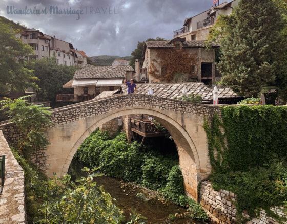 A tone bridge over a small river with Alex standing the middle waving, a romantic spot for a photo