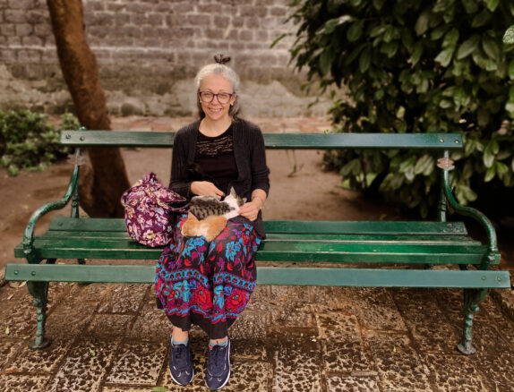 Bell sits on a park bench with a black, tabby and ginger kitten on her lap