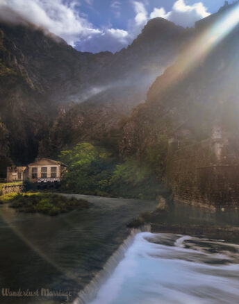 A river flowing at the foot of the mountains, with sun shinning through as the clouds part after a storm