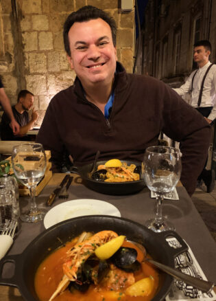 Two plates with seafood and Alex is smiling for the photo as a server hustles behind him.