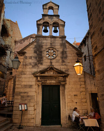 Old stone chapel at dusk with people sitting at a table enjoying dinner