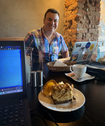 Alex smiles with his laptop in front of him as well as a delicious piece of cake