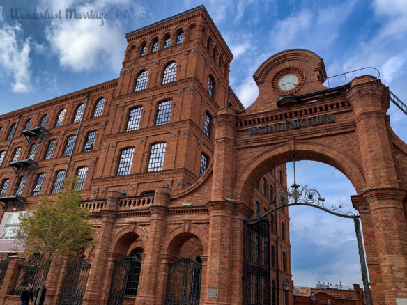 Red brick manufaktura building with arched entrance and blue skies